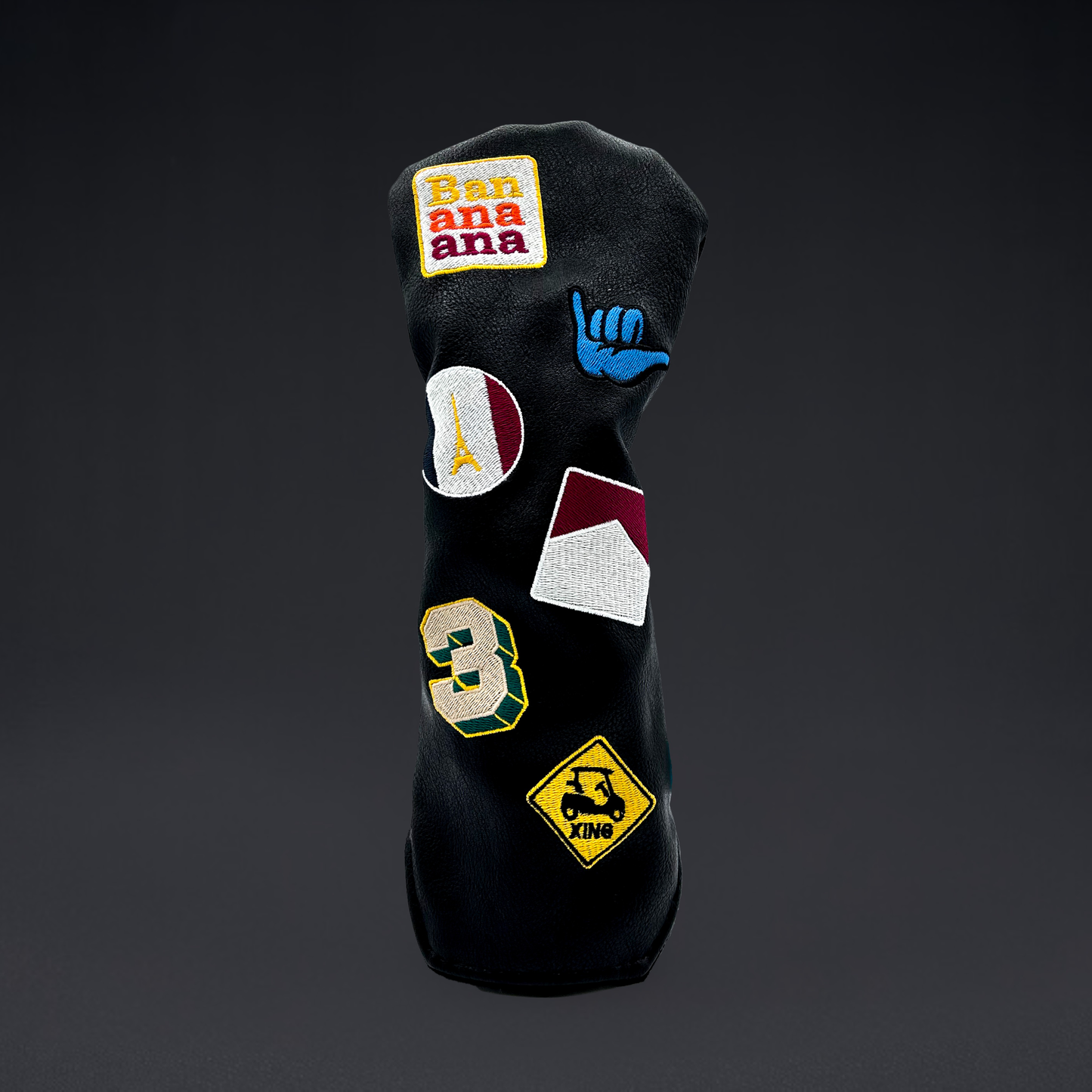 Black golf club wood head cover with custom patches on black backdrop