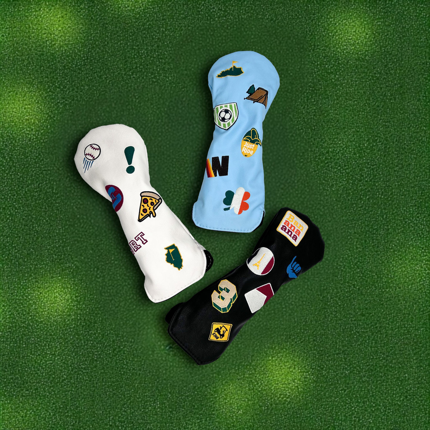 Three wood golf club head covers with custom patches laying on green turf