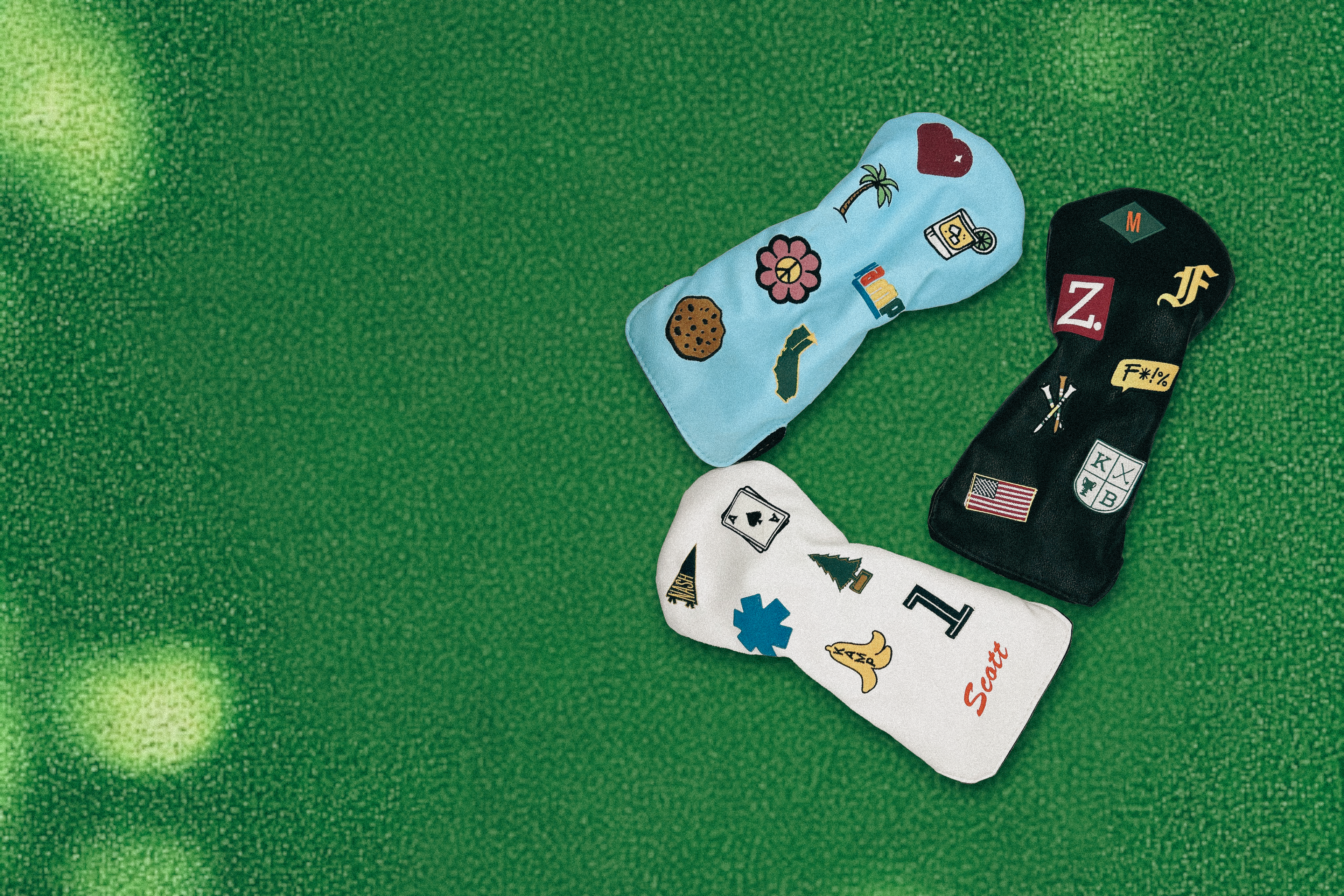 Three driver golf club head covers with custom patches laying on green turf