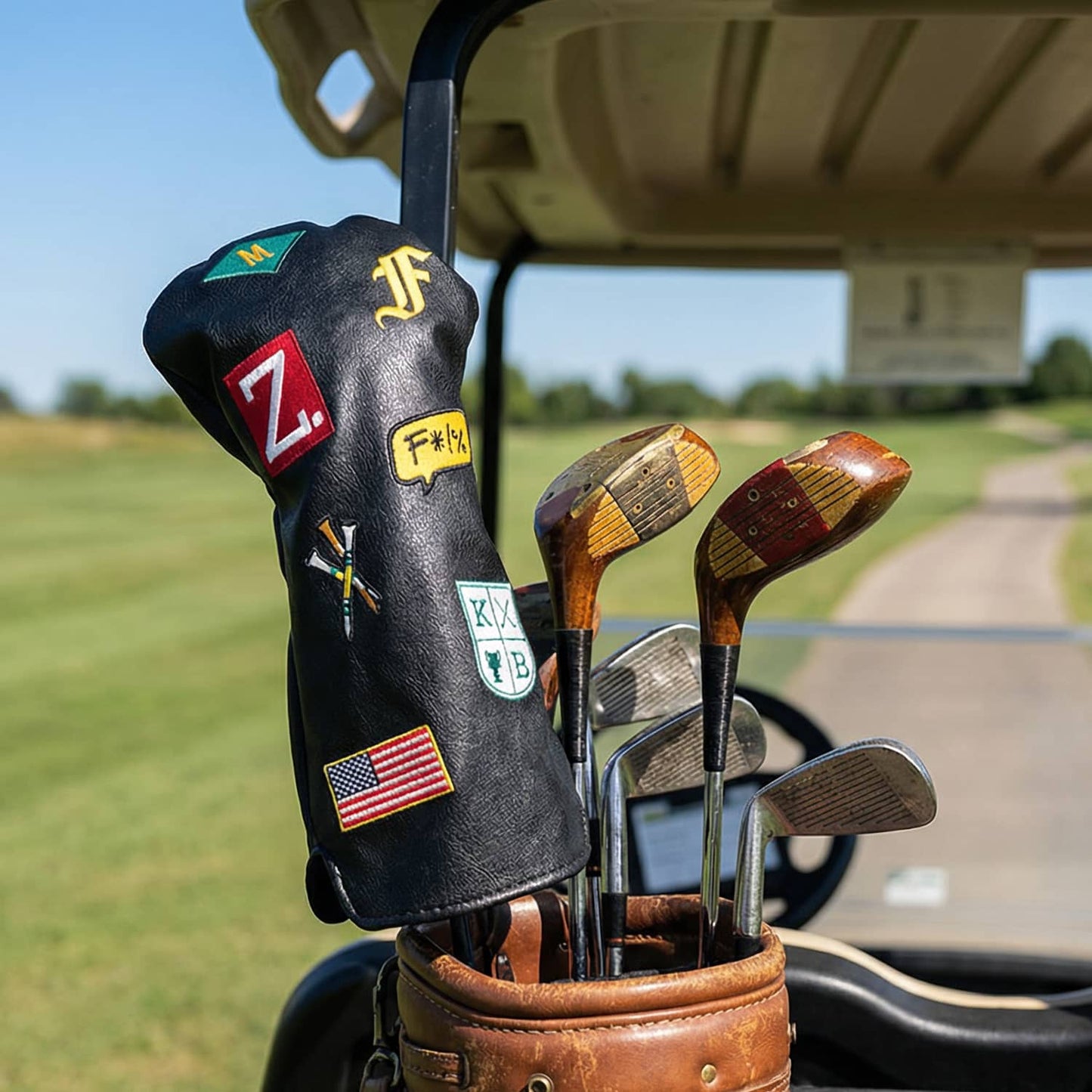Custom black golf driver head cover with letter monograms M, F, and Z, crossed golf tees, American flag, and country club crest patches on vintage leather golf bag at golf course - personalized driver cover by KAMP BANANA