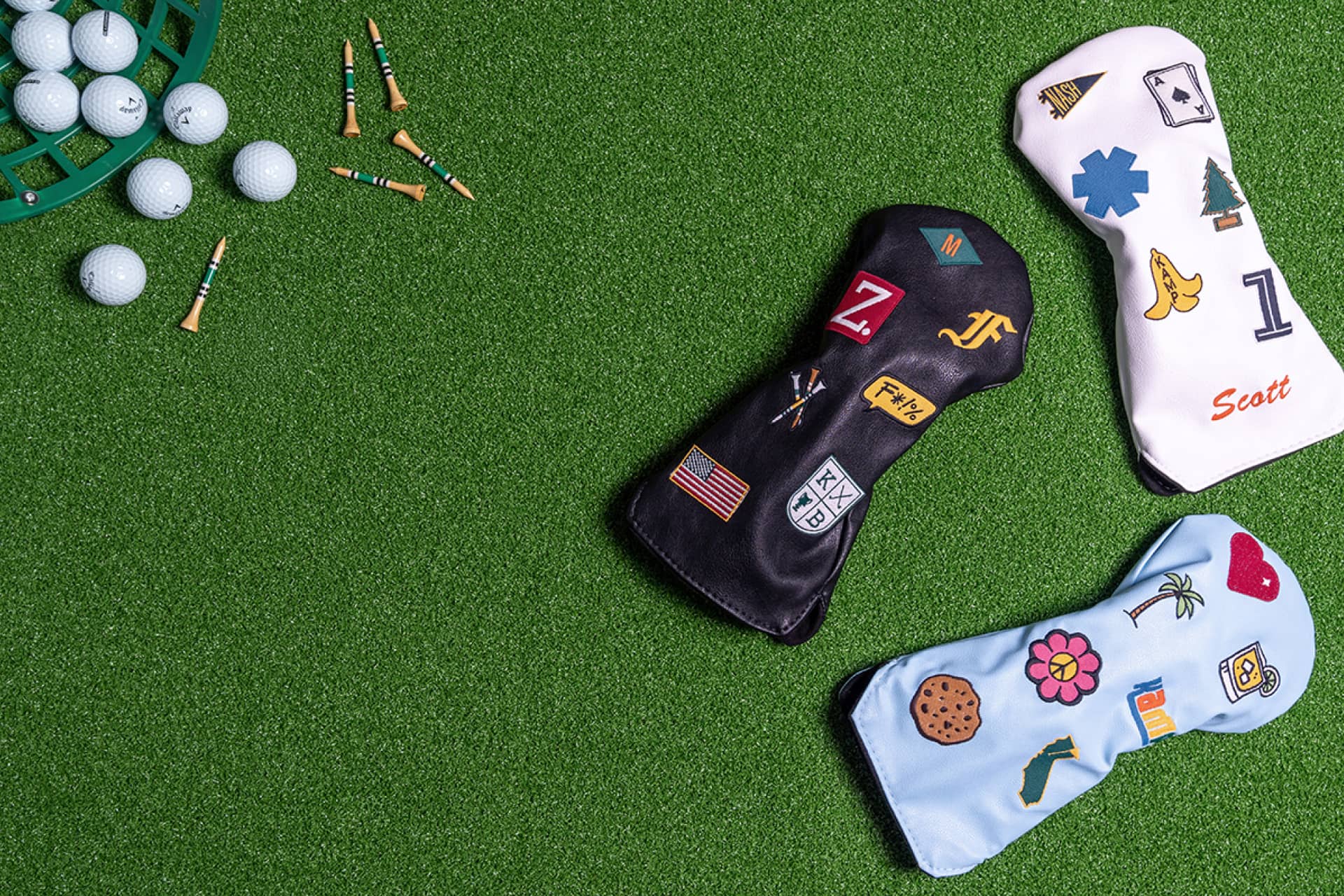 Custom golf head covers in black, white, and light blue with personalized embroidered patches displayed on green turf with golf balls and tees - featuring Scott name monogram, Nashville pennant, ace of spades, American flag, hibiscus flower, and cookie patches - KAMP BANANA handmade golf club covers