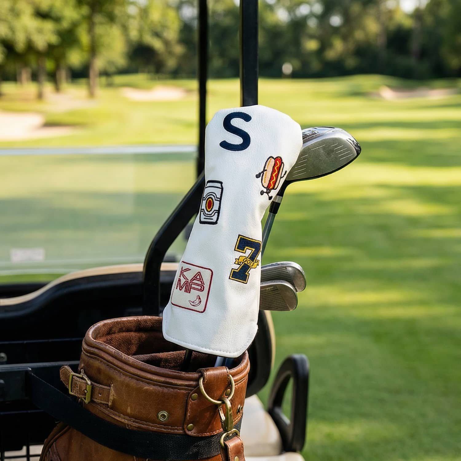 Custom white hybrid golf head cover with S monogram, hot dog patch, number 7, and KAMP logo on leather golf bag at golf course - personalized driver cover in use on the course - handmade vegan leather