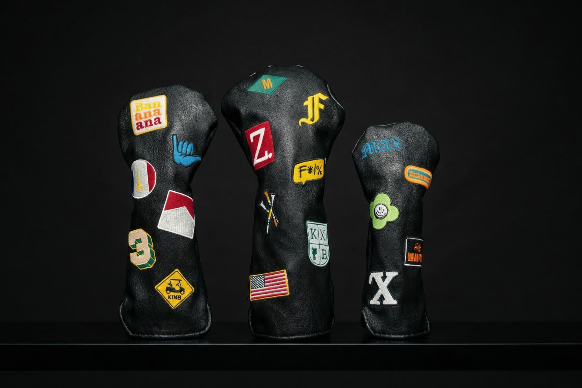 Collection of personalized golf head covers in black featuring custom patches, state flags, monograms, and hobby-themed embroidery