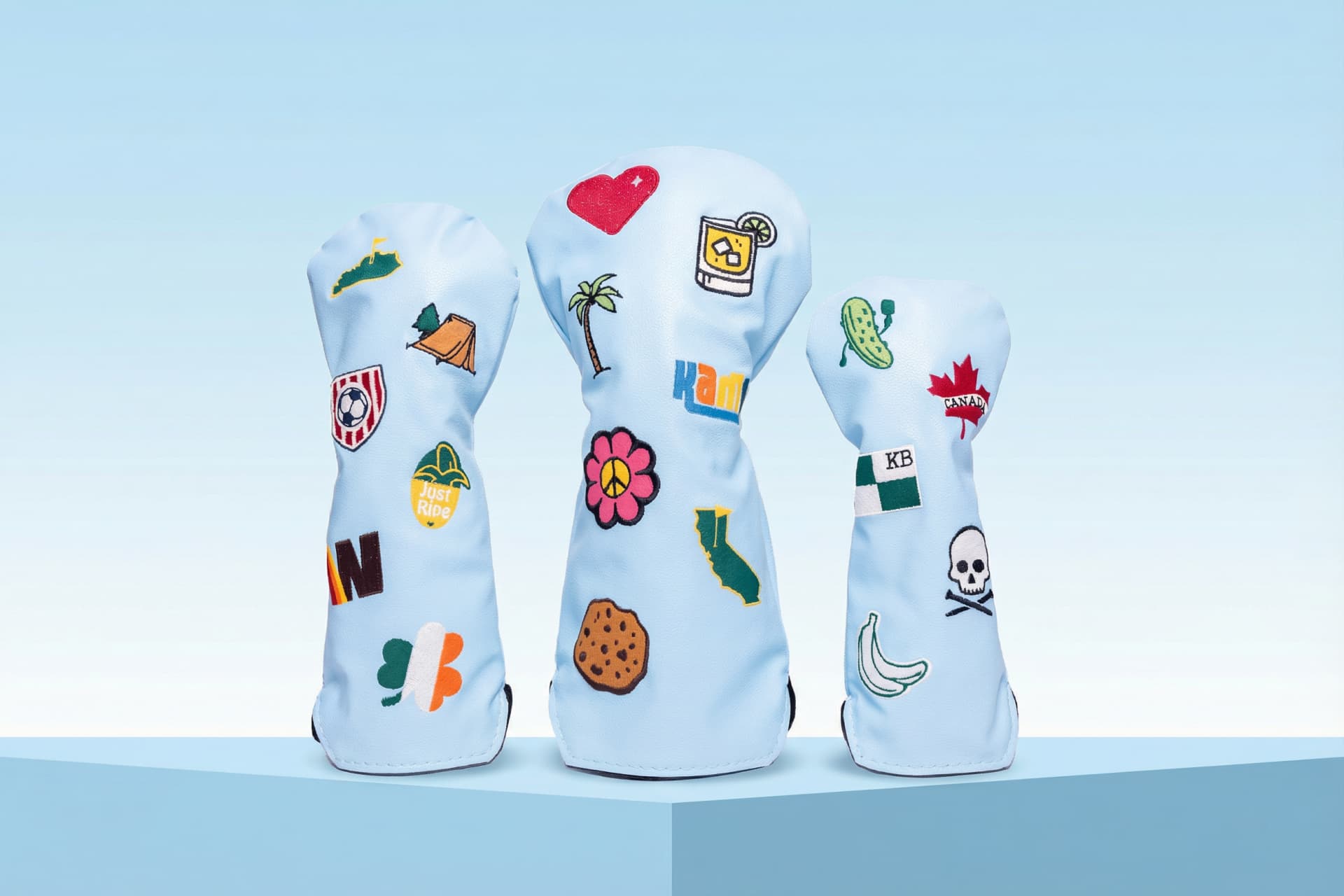 Collection of personalized golf head covers in light blue featuring custom patches, state flags, monograms, and hobby-themed embroidery