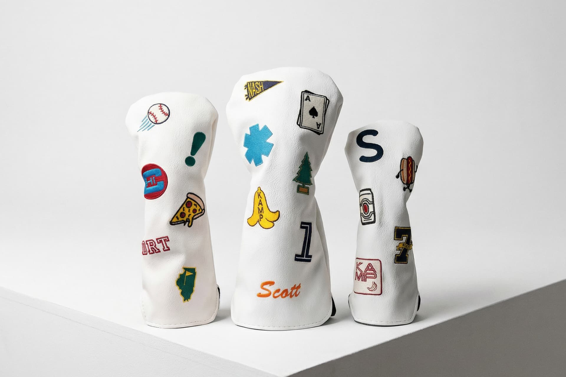 Collection of personalized golf head covers in white featuring custom patches, state flags, monograms, and hobby-themed embroidery