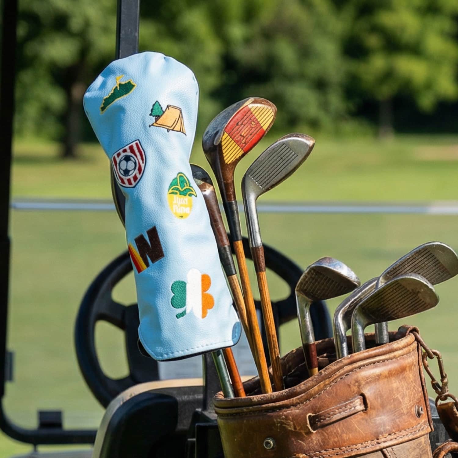 Custom light blue golf fairway wood head cover with Kentucky state, camping tent, soccer crest, Irish shamrock, and letter N patches on vintage leather golf bag at golf course - personalized driver cover by KAMP BANANA