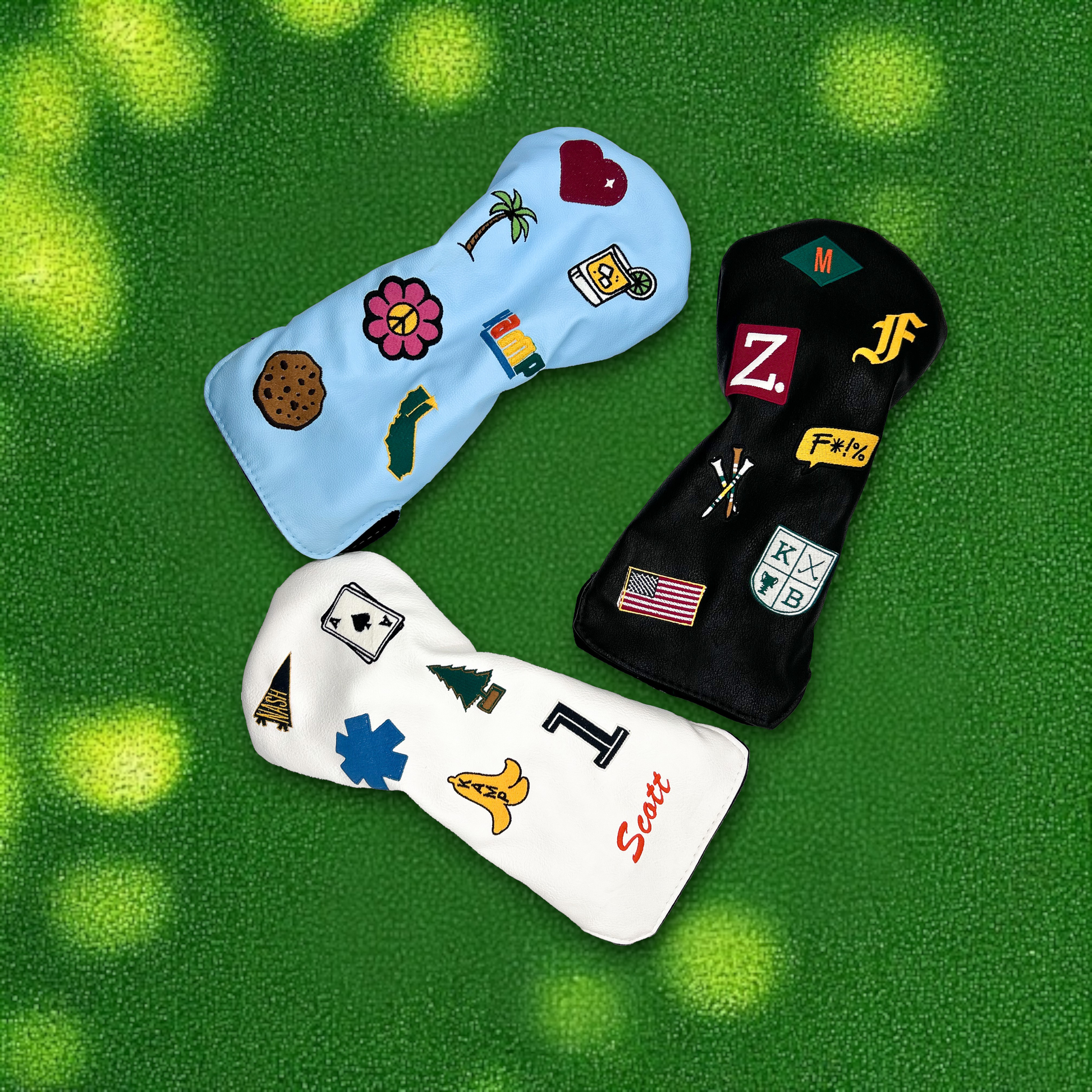 Three driver golf club head covers with custom patches laying on green turf