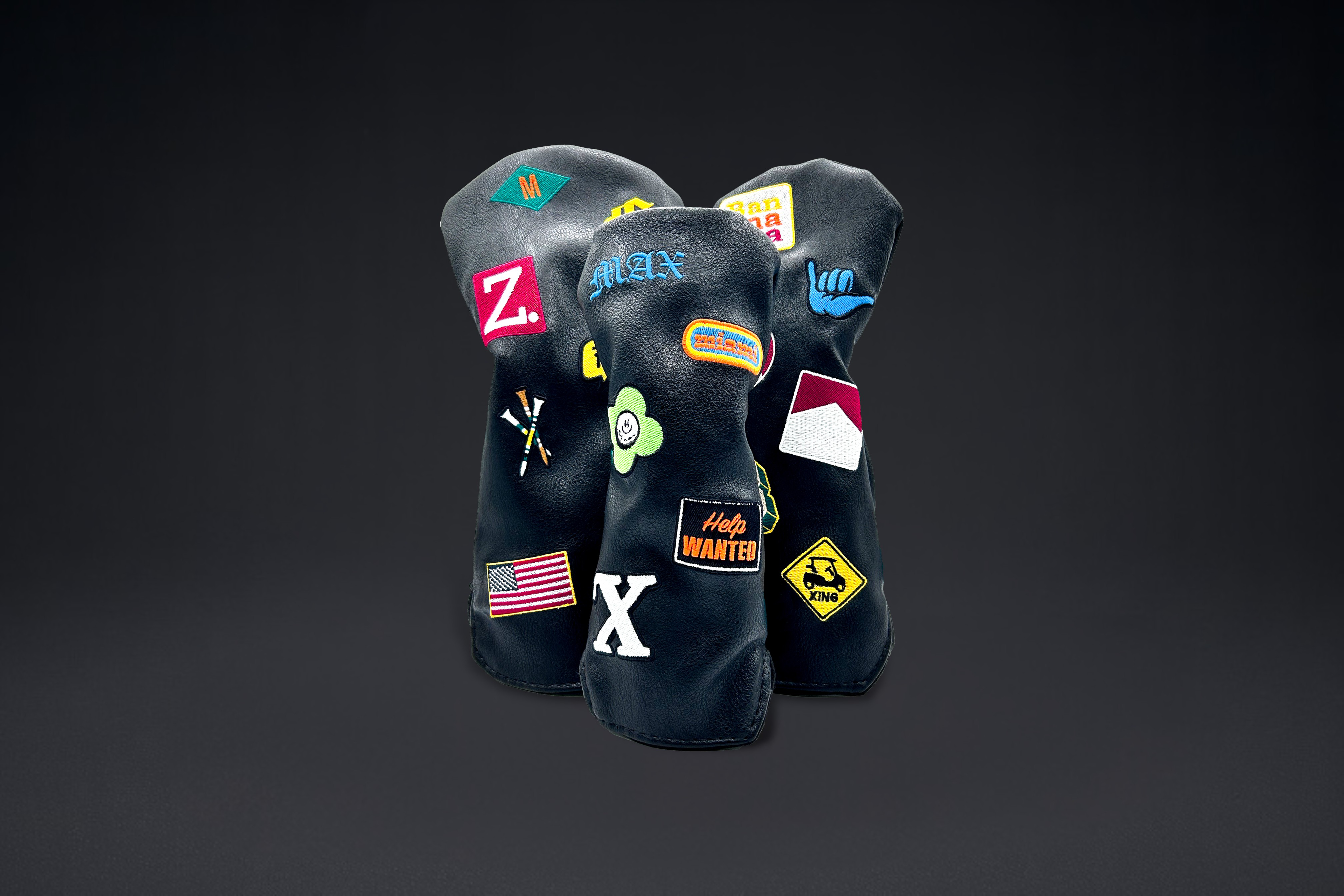Three black golf club head covers with custom patches on black backdrop